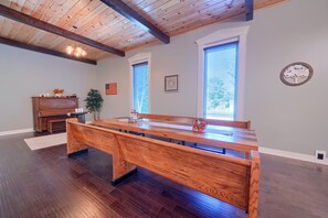 Una habitación amplia con un banco de madera, un piano y un ventanal con persianas.