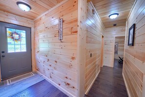 Un pasillo interior de madera con un cartel de bienvenida, una puerta gris y un cuadro en la pared.