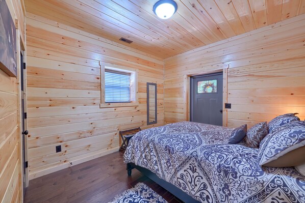 A wooden-paneled room with a bed, a door with a window, and a ceiling light.