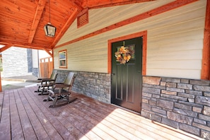 A wooden deck with rocking chairs, a stone wall, and a door with a wreath.