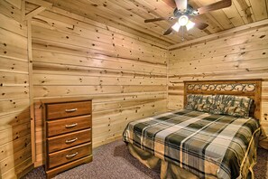 Ein Schlafzimmer mit Holzwänden, einem Bett, einer Kommode und einem Deckenventilator.