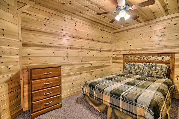 A wooden-paneled bedroom with a bed, a dresser, and a ceiling fan.