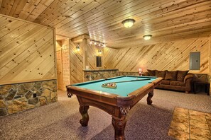 Ein Billardtisch in einem Raum mit Holzboden, Steinverzierungen und einem braunen Sofa.