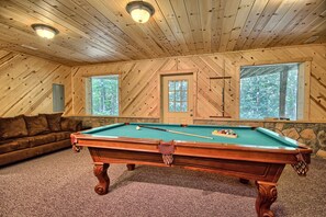 Una sala con paneles de madera, una mesa de billar, un sofá de cuero marrón y una pared de piedra.