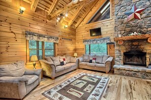 A log cabin interior with a stone fireplace, wooden walls, and a cozy seating area.
