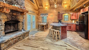 A log cabin interior with a stone fireplace, wooden dining table, bar area, and kitchen. - Double Pine Lodge - 5 Bedroom -Hocking Hills (Logan)