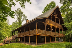 A large wooden cabin with a balcony, surrounded by trees.