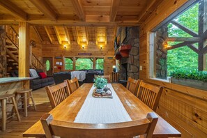 Een houten cabin met een eettafel, stoelen, een bank en een trap.