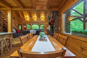 Ein Holzblockhaus-Interieur mit Esstisch, Stühlen, einer Couch und einer Treppe.