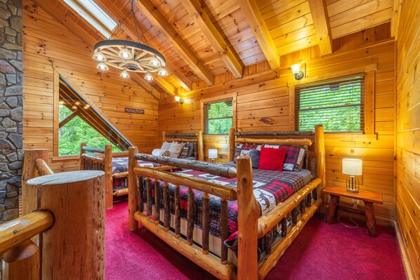 A log cabin room with a wooden bed, a stone wall, and a window with blinds.