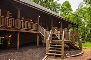 A wooden cabin with a porch, a staircase, and a view of the surrounding forest.