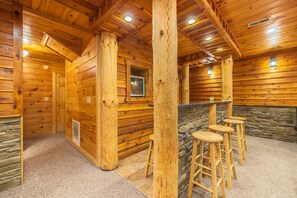 A wooden interior with a stone accent wall, wooden columns, and a bar area with stools. - Timber Ridge Lodge - 5-BR, w/King Suite - Hocking (Logan)