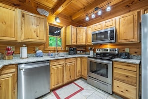 Une cuisine rustique, située dans une cabane en bois, équipée d’un lave-vaisselle, d’une cuisinière, d’un four à micro-ondes et de meubles de rangement en bois.