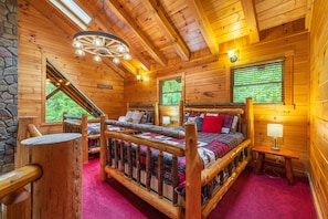 A log cabin room with a wooden bed, a stone wall, and a window with blinds.