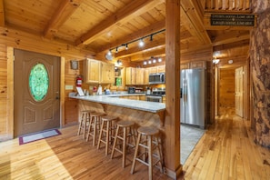 A wooden cabin interior with a kitchen, bar stools, and a sign with motivational phrases.