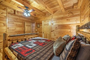 Ein Holzblockhaus-Interieur mit Bett, Deckenventilator und einem rustikalen Holz-Kopfteil.