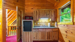 L’intérieur d’une cabane en bois comprend un coin cuisine, un four à micro-ondes, un réfrigérateur, un évier et une fenêtre donnant sur un paysage verdoyant.