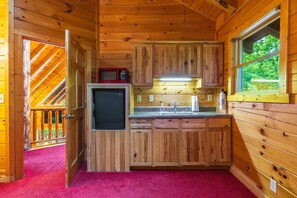 A wooden cabin interior with a kitchenette, a microwave, a refrigerator, a sink, and a window with a view of greenery. - Timber Ridge Lodge - 5-BR, w/King Suite - Hocking (Logan)