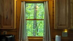 Ikkuna, jossa on verhot, puuseinät ja näkymä metsään.
