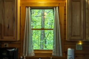 A window with curtains, wooden walls, and a view of a forest. - Hunter's Retreat - Cozy Cabin, near Old Man's Cave (Logan)