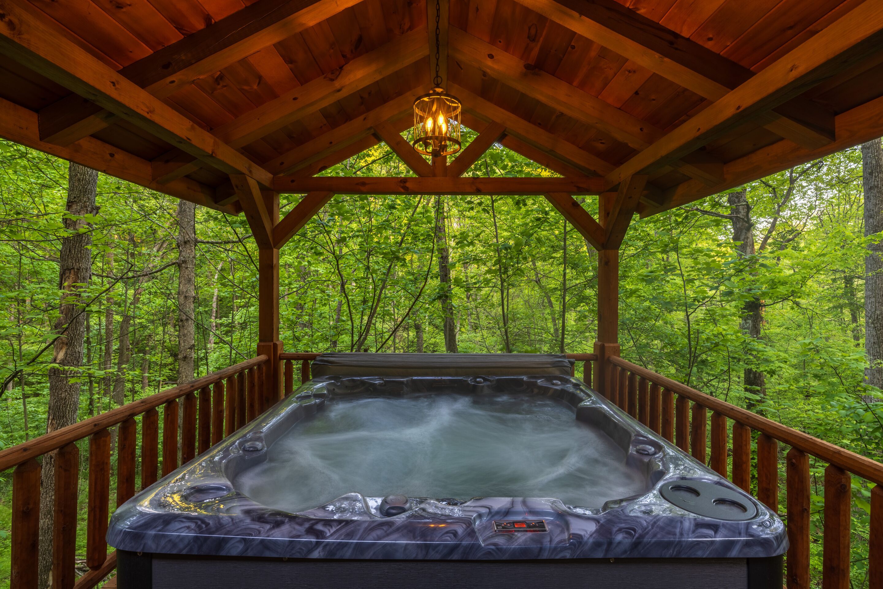 A hot tub in a wooden gazebo surrounded by a forest.