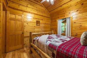A wooden cabin room with a bed, wooden walls, a window, and a door.