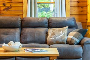 A brown leather sofa with a bowl of snacks and a magazine on a wooden table.