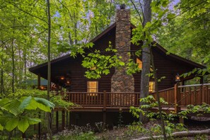 A log cabin with a stone chimney, wooden deck, and surrounded by trees. - Hunter's Retreat - Cozy Cabin, near Old Man's Cave (Logan)