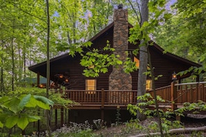 A log cabin with a stone chimney, wooden deck, and surrounded by trees. - Hunter's Retreat - Cozy Cabin, near Old Man's Cave (Logan)