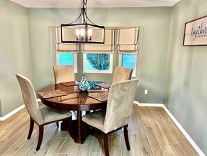 A dining area with a round table, four chairs, a chandelier, and a window with a view of trees. - Covered Heated Pool Included! Only 12 Min Drive to Beach! (Englewood)