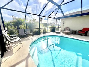 A covered swimming pool with a clear view of the surrounding landscape, including palm trees and a house in the background. - Covered Heated Pool Included! Only 12 Min Drive to Beach! (Englewood)