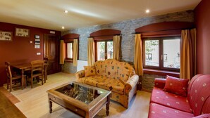 A cozy living room with a sofa, a red armchair, a wooden coffee table, and a dining area with a table and chairs. - Hotel rural los Cerezos (Yanguas)