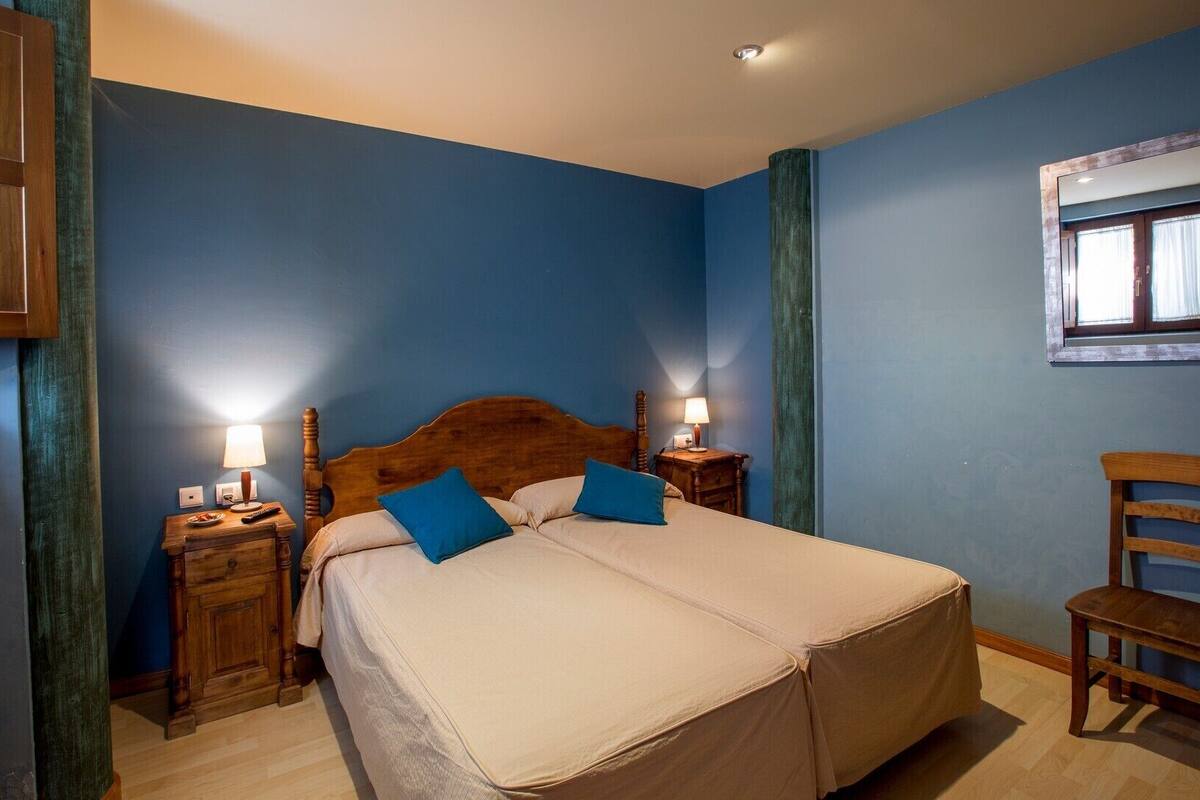 A bedroom with a large bed, two bedside tables with lamps, a wooden chair, and a window with curtains.