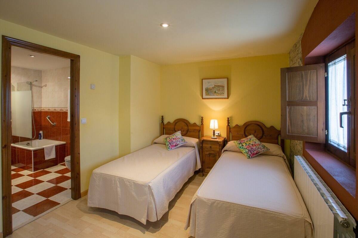 A room with two beds, a bathroom with a checkered floor, and a window with curtains.