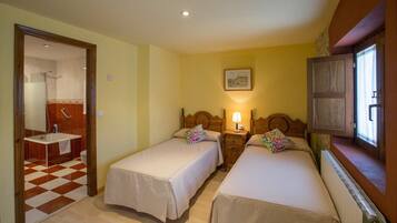 A room with two beds, a bathroom with a checkered floor, and a window with curtains.