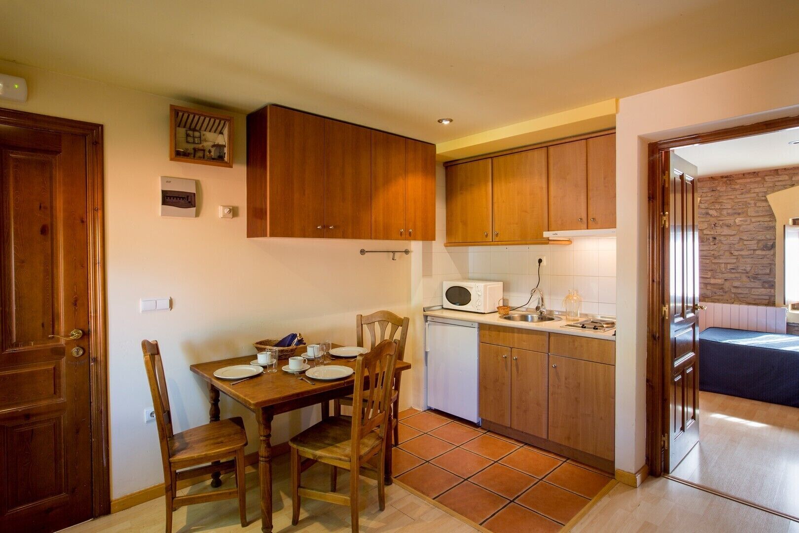 Una cocina compacta con armarios de madera, una mesa de comedor con sillas, un microondas y un refrigerador pequeño.