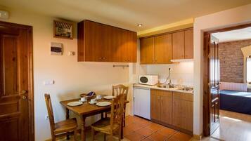 Una cocina compacta con armarios de madera, una mesa de comedor con sillas, un microondas y un refrigerador pequeño.