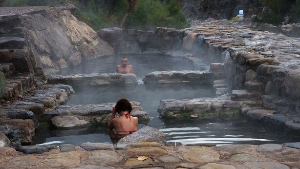 A natural hot spring with rocky surroundings and a person sitting in the water. - Hotel rural los Cerezos (Yanguas)
