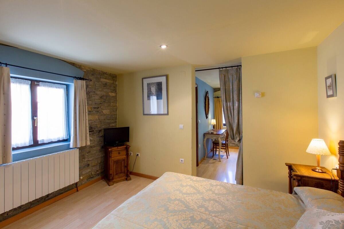 A bedroom with a bed, a TV, a desk with a chair, a lamp, and a mirror.