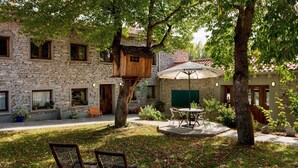 A stone building with a wooden treehouse, outdoor seating, and a patio area. - Hotel rural los Cerezos (Yanguas)