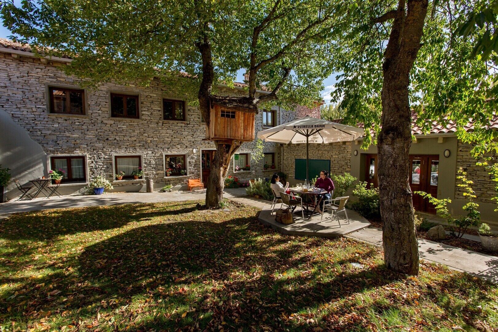 Un edificio de piedra con una casa del árbol, mobiliario exterior y una zona de patio.