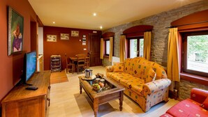 A cozy living room with a sofa, a coffee table with fruits and glasses, a TV, and a dining area with chairs and a table. - Hotel rural los Cerezos (Yanguas)
