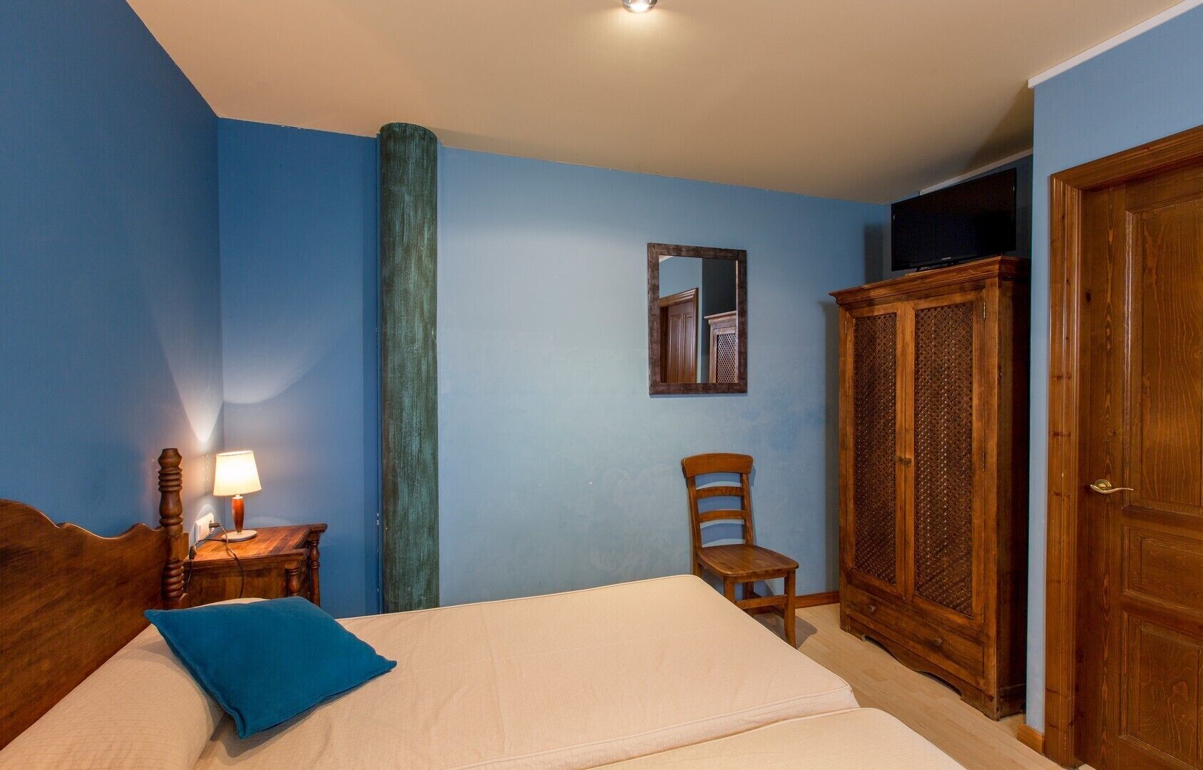 Un dormitorio con cama, una silla, armario de madera, espejo y lámpara.