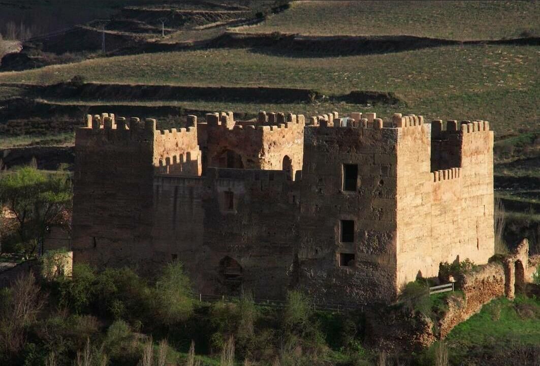 A medieval castle with multiple towers and a fortified wall, surrounded by grassy hills.