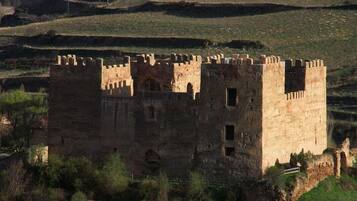 A medieval castle with multiple towers and a fortified wall, surrounded by grassy hills.