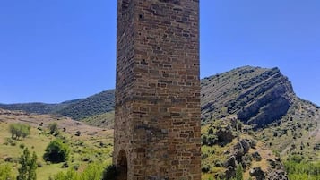 Una torre de piedra alta y esbelta con aberturas arqueadas, con colinas onduladas y un cielo azul despejado de fondo.