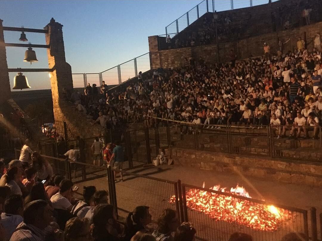 A crowded outdoor amphitheater with tiered seating and a central fire.