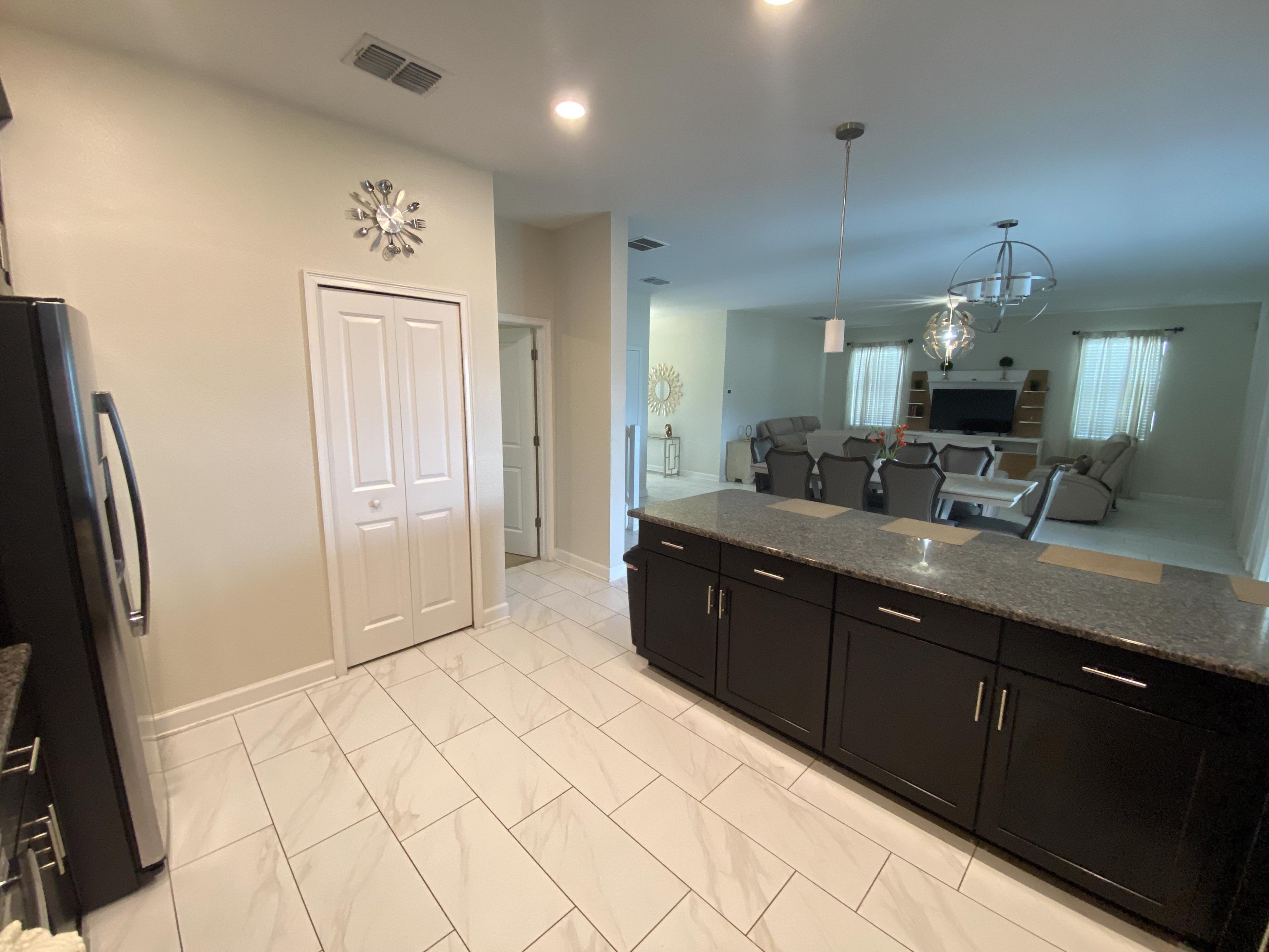 A modern kitchen with dark cabinets, a granite countertop, and a white tiled floor.