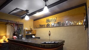 A reception area with a stone counter, a wooden sign reading "Hotel Jardines de Mallku Cueva," and a decorative vase with red flowers.