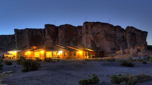 A lodge with a large rock formation backdrop, outdoor lighting, and a vehicle parked in front.